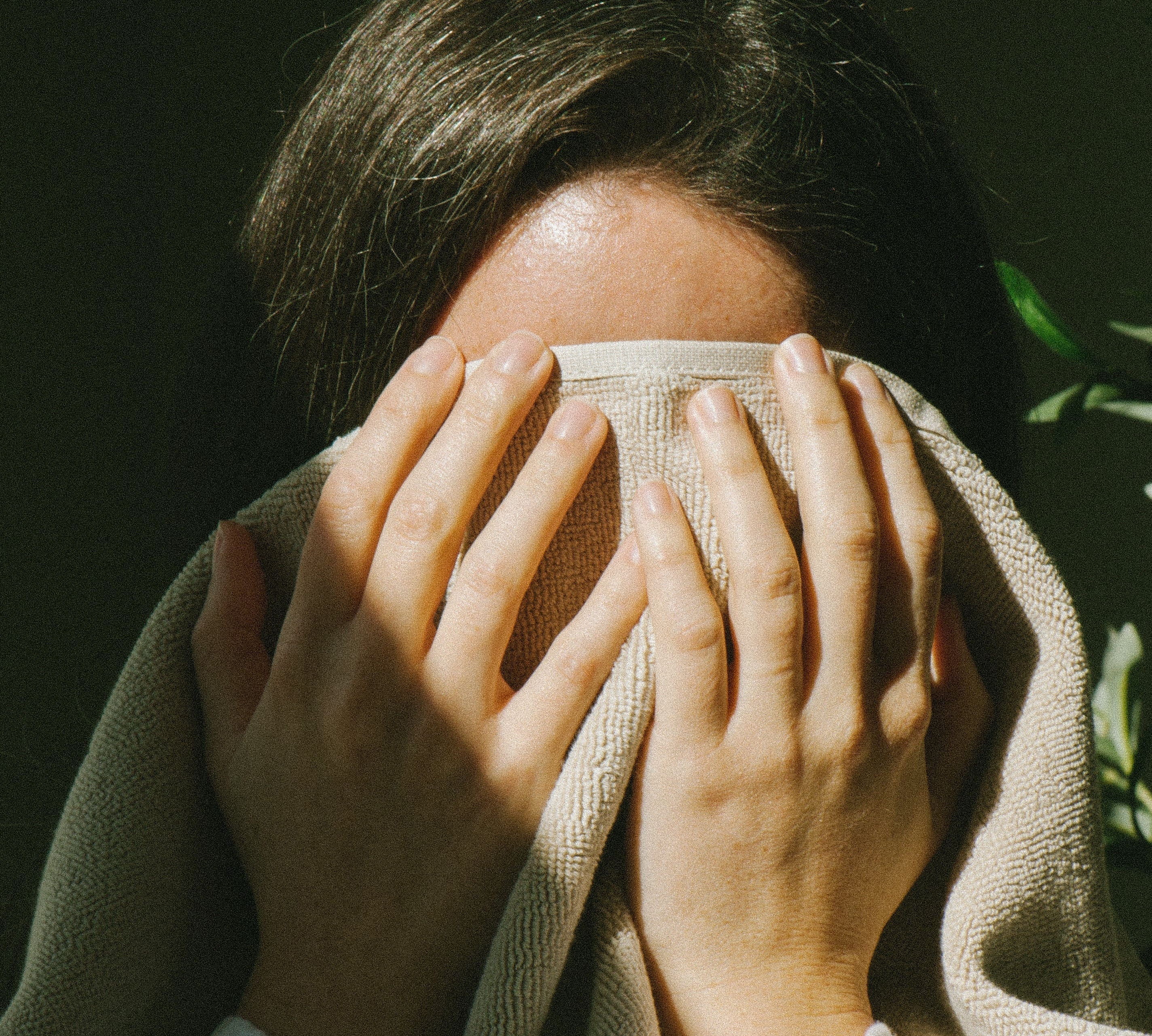 Person with brown hair drying their wet face from cleaning with a dry towel, their hands and towel in front to cover their face