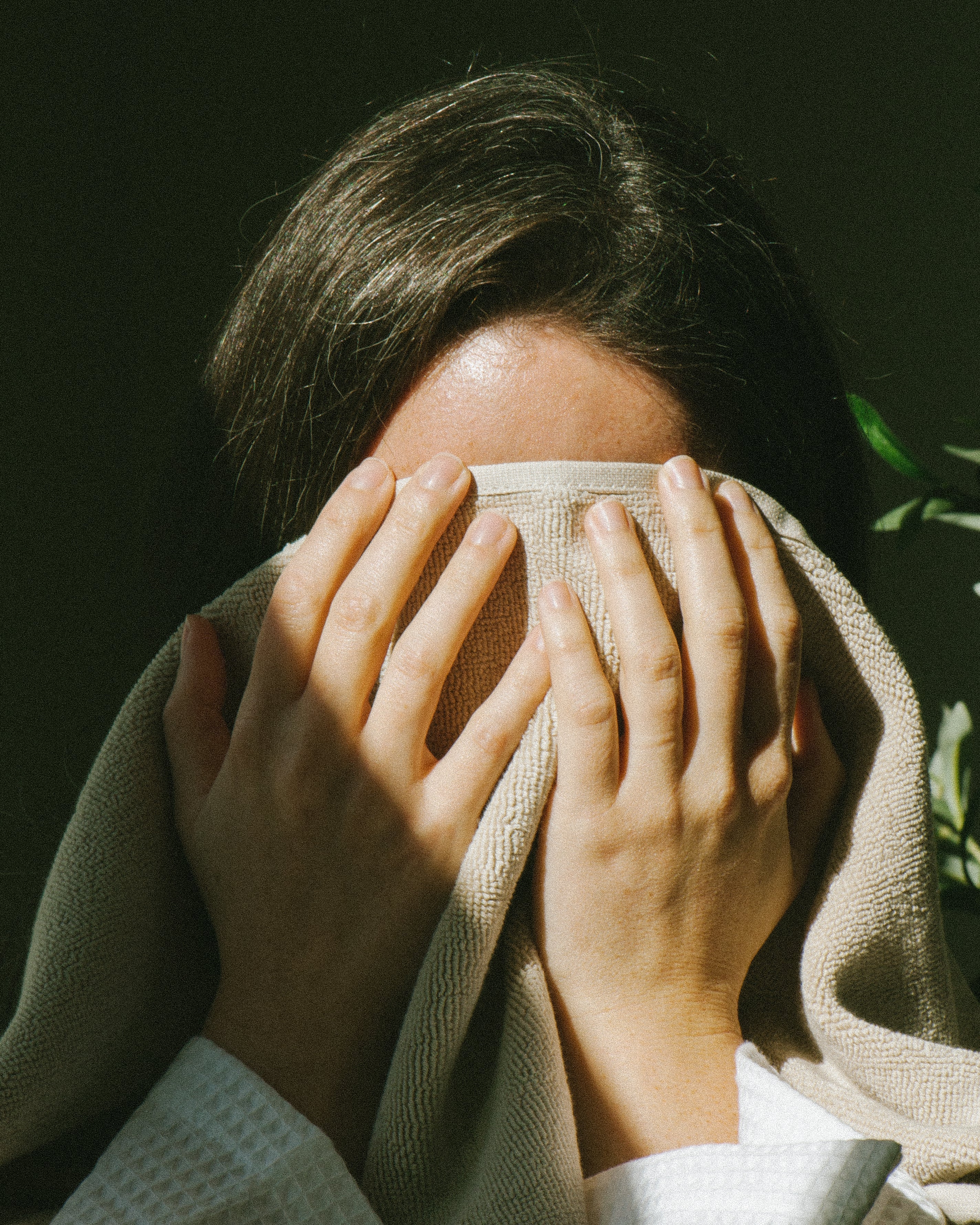 Person with brown hair drying their wet face from cleaning with a dry towel, their hands and towel in front to cover their face
